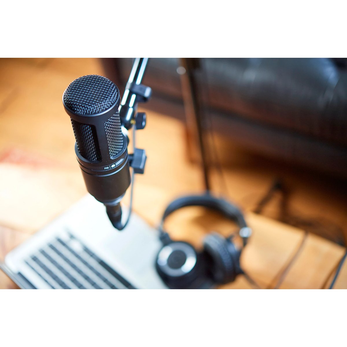 AT2020 microphone set up on boom arm above a laptop with headphones on desk