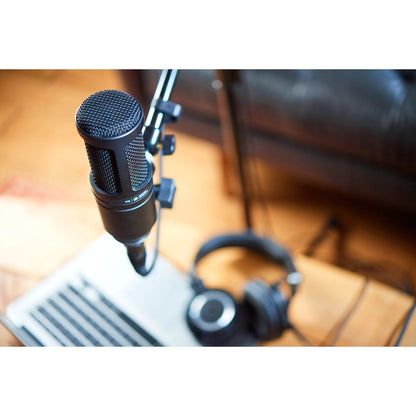 AT2020 microphone set up on boom arm above a laptop with headphones on desk