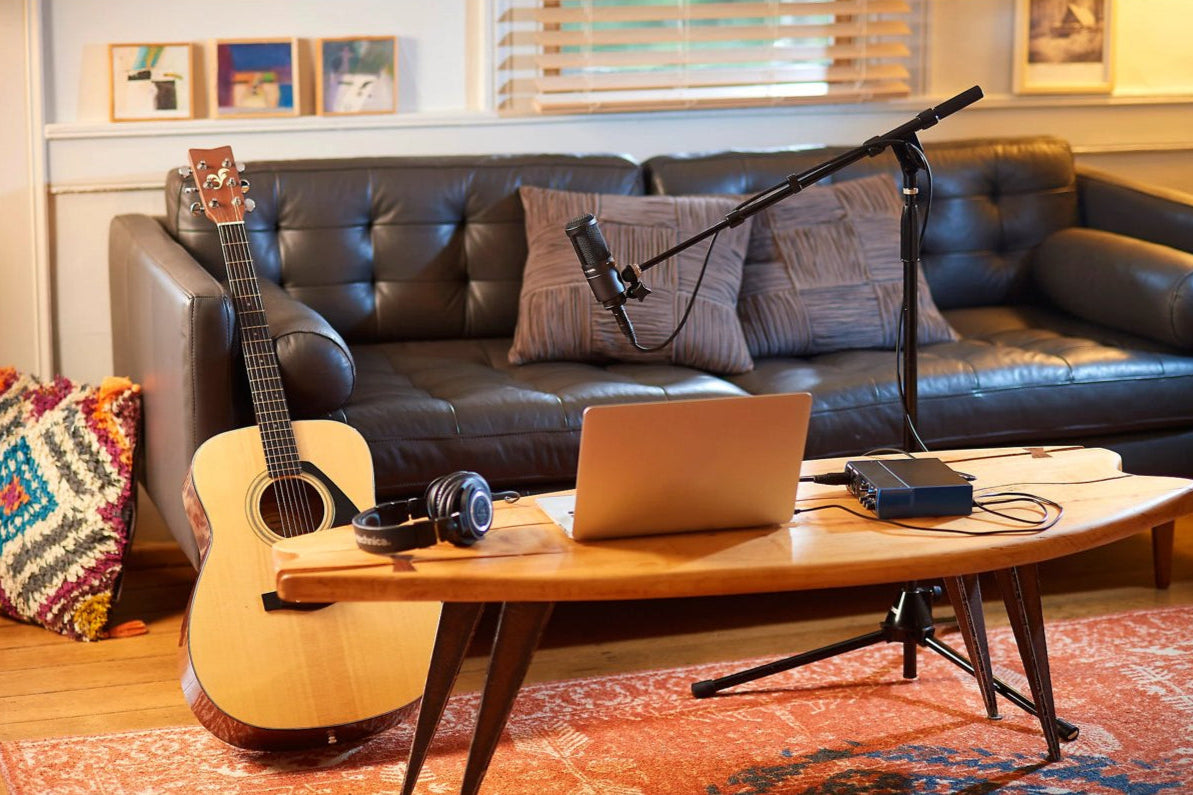 AT2020 home recording setup with laptop, guitar, headphones, and audio interface on a wooden table