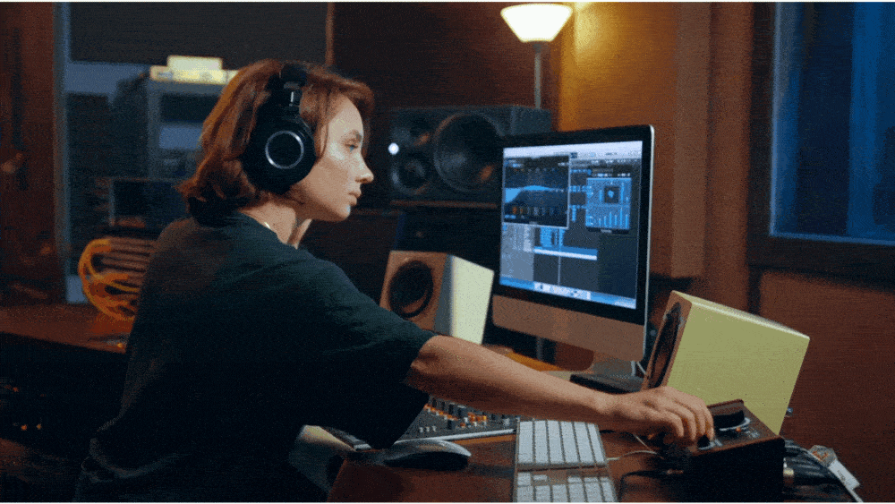 Studio engineer wearing headphones adjusting gear while working with audio software on a desktop monitor at Pro Audio Clinic